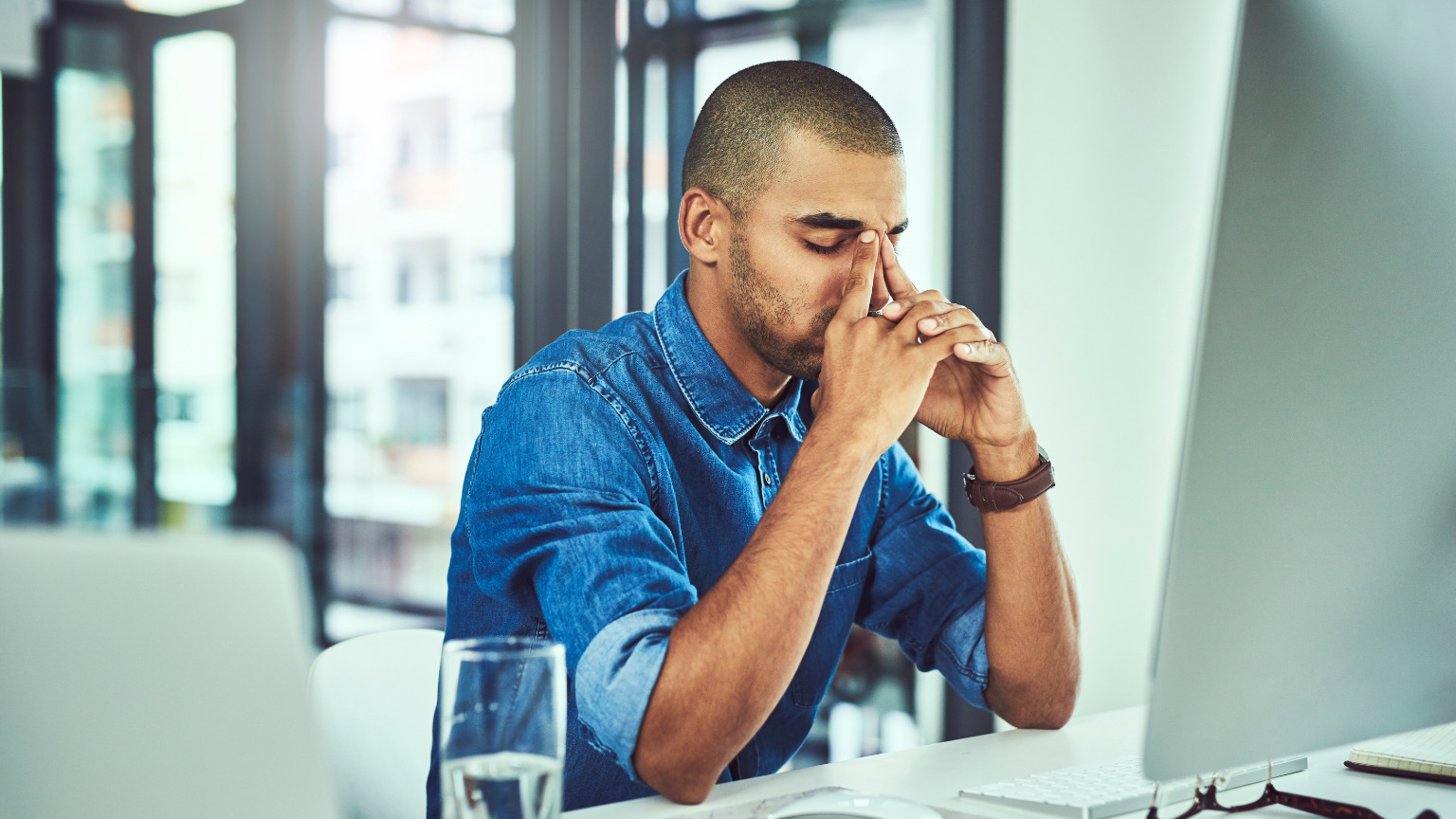 A man sits at his desktop computer, overwhelmed with his hands on his face.